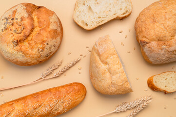 Bread background. Fresh white wheat bread, round classic, ciabatta, french baguette, wheat ears and grains on beige background flat lay top view. Bread making, bakery, healthy food. Light mockup