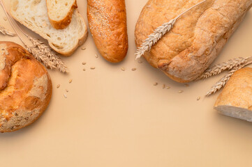 Bread background. Fresh white wheat bread, round classic, ciabatta, french baguette, wheat ears and grains on beige background flat lay top view. Bread making, bakery, healthy food. Light mockup