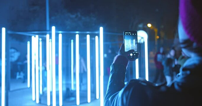 Beautiful woman recording video of neon lights performance show at night with smartphone. Photography, video, lights entertainment and technology concept. High quality 4k footage