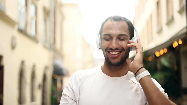 Portrait of smiling young African American man listening to music in headphones. Closeup face of attractive guy in the city centre.