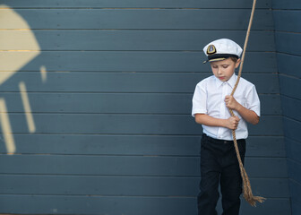 Little ship captain on the deck of the ship. The boy stands leaning on rope ladders. The boy looks into the distance