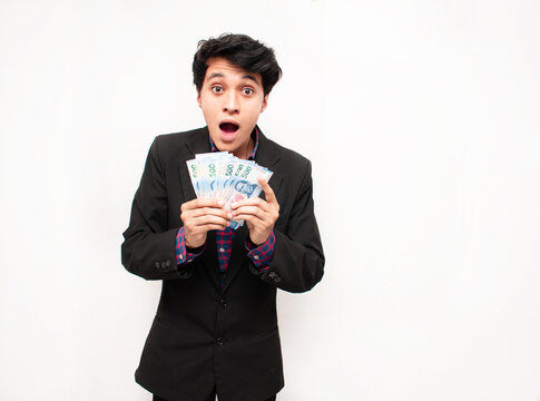 Joven hombre vestido de traje sosteniendo billetes en sus manos y mostrando cara de sorprendido sobre un fondo blanco