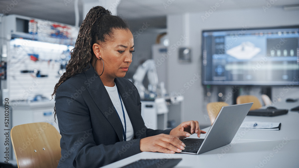 Poster At the Factory: Black Automation Engineer Uses Laptop for Programming Robotic Arm while Sitting at Table and then Going to Robot. New Era in Automatic Manufacturing Industry Concept.