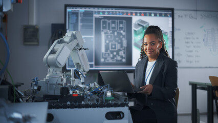 Portrait of Smiling Black Developer Using Laptop while Working with Robotic Arm in Modern...