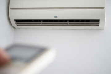 An unrecognizable person holding the remote control in front of the air conditioner at home