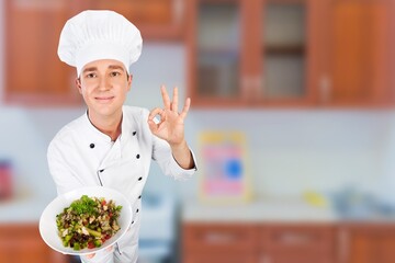 Young man standing and holding plate or dish on kitchen background