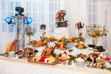 Buffet table with meat snacks, baked pigs in dough, cheese, turkey with fruit, decorated with candelabra and gramophone