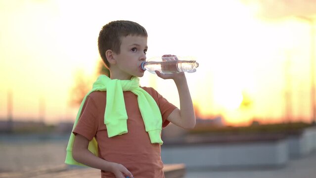 Young man drinking water from a plastic bottle in the city at sunset