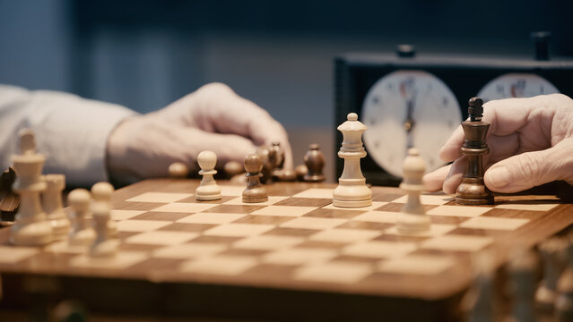 partial view of senior men playing chess on blurred chessboard