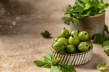 Fresh gooseberry in ceramic bowl with mint and beautiful bokeh of water drops on beige textured background with copy space