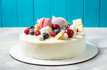 Tender white cake decorated with melted white chocolate, macaroons, berries and candies on concrete background.