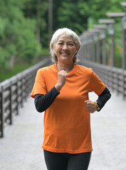 A retired Asian woman wearing an orange T-shirt is exercising outdoors, running, lifting dumbbells, stretching.