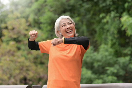 A retired Asian woman wearing an orange T-shirt is exercising outdoors, running, lifting dumbbells, stretching.