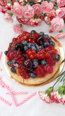 Berry birthday cake. Cheesecake with cherries, raspberries, currants and blueberries. Cake, pink candles and red flowers on a white background. Photo for stories.