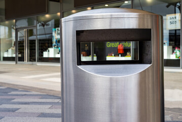 Close up of shiny silver chrome public waste bin, ashtray, located on urban shopping centre street.