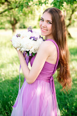 Naklejka premium Portrait of a young girl in a light purple dress with a bouquet of peonies in her hands. Graduation, bridesmaid posing in the garden.