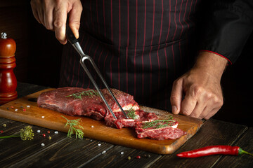 An experienced chef prepares raw fresh beef meat for roasting or barbecue. Working environment in the kitchen of a restaurant or hotel.
