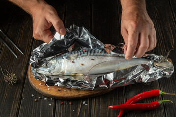 Before baking, fresh fish must be wrapped in foil. Close-up of chef hands while cooking delicious...