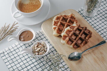 Croffle, Croissant Waffle Korea pastry. Croffle served in wooden plate with almonds, chocolate sauce and coffee on square pattern table cloth. Selective focus.