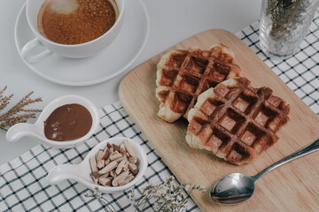 Croffle, Croissant Waffle Korea pastry. Croffle served in wooden plate with almonds, chocolate sauce and coffee on square pattern table cloth. Selective focus.