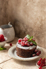 Chocolate cake with red summer berries sprinkled with powdered sugar on beige tile background. Beautiful still life, text space