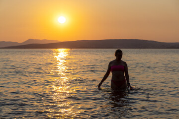 A girl is standing in the sea during sunset, the Adriatic Sea in Croatia