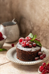 Chocolate cake with red summer berries, mint leaves and powdered sugar close up on beige tile background. Cozy still life, text space