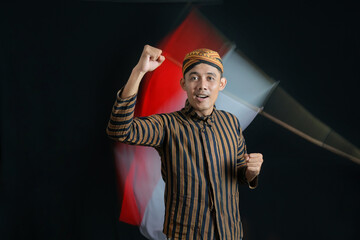 Young Asian man wearing traditional batik clothes showing the richness of Indonesian culture in independence month against the background of the Indonesian national flag