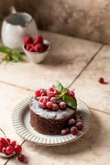Chocolate cake with red summer berries, mint leaves and powdered sugar on beige tile background