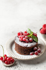 Chocolate cake with red berries, mint leaves and snowy powdered sugar close up on white textured background with copy space