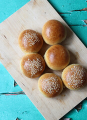 Home baked buns with sesame seeds on wooden board. Close up photo of crusty sourdough buns. 