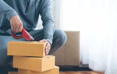 Detail of packing cardboard boxes while moving house.  Young man packing box, indoors young male warehouse worker packing boxes for shipment. 