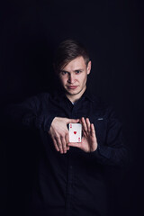 Confident young man showing tricks with playing cards like a magician, isolated on dark background....