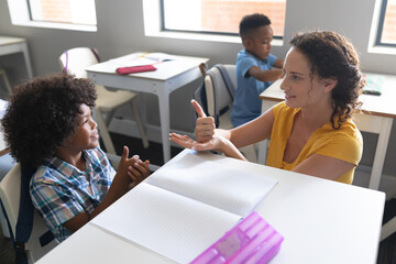 Caucasian young female teacher teaching sign language to african american elementary boy in class