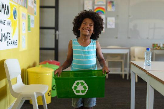 Smiling african american elementary schoolboy holding container with recycle symbol