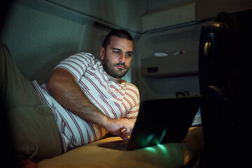 Truck driver using laptop while relaxing in cabin at night.