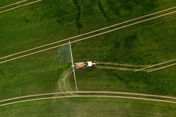 aerial view of the tractor spraying the chemicals on the large green field - Powered by Adobe
