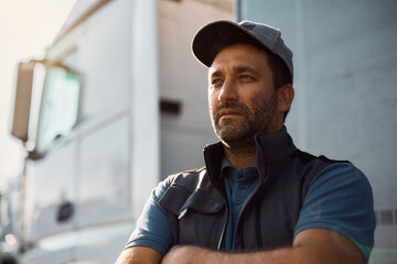 Pensive truck driver in front of his vehicle looking away,