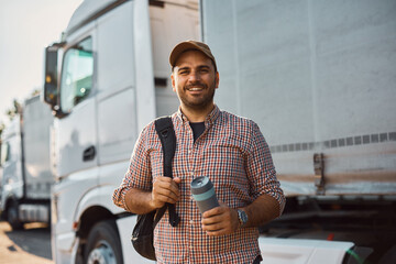Young happy truck driver on parking lot looking at camera.