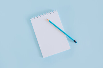 Notebook with blank page and pencil on light blue background.