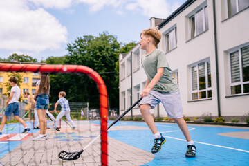 Group of children playing street hockey on a city holiday on the playground. Summer activites for children concept.