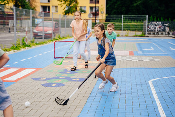 Funny girl hockey player hitting ball with hockey stick on the playground outdoor. Summer activites for children concept.