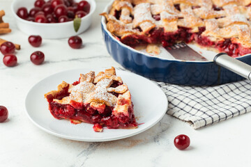 Piece of delicious homemade cherry pie with Flaky Crust sprinkled with powdered sugar on the white marble background. American traditional cherry tart.