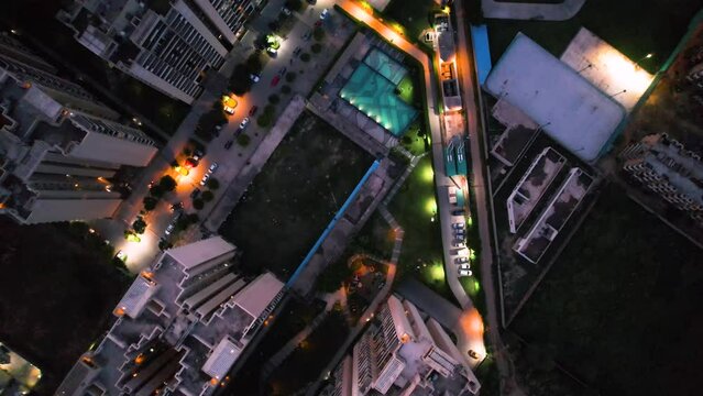 aerial drone shot at dusk twilight in gurgaon delhi looking straight down at skyscrapers buildings of a premium apartment complex with a pool, parking and panning up to reveal the city skyline