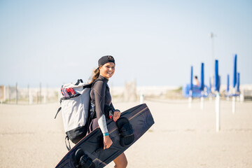 Beautiful girl smiling and comes to the beach with kitesurfing equipment - Sporty woman concept and...