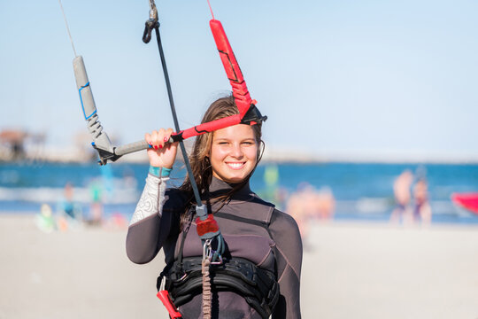 Portrait of a young kitesurfer girl walking upwind at the beach with her board and a kite. A young female kite surfer ready for kite surfing competitions