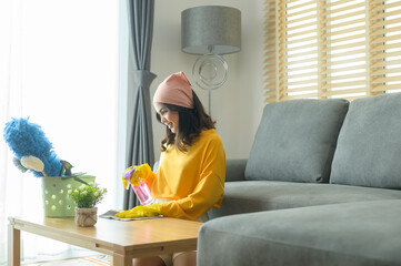 Fototapeta na wymiar Young happy woman wearing yellow gloves and dusting the table in living room.
