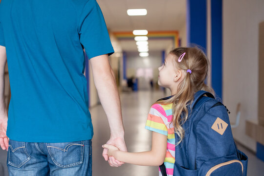 Back to school. Child with father holding hands in school hallway. Happy kid going to first grade. Little girl with backpack indoors. Concept of confidence, support, togetherness. First day at school