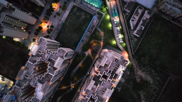 aerial drone shot showing height gain looking down over skyscrapers of a premium apartment complex with parking swimming pools with lights switched on at dusk twilight in gurgaon haryana India