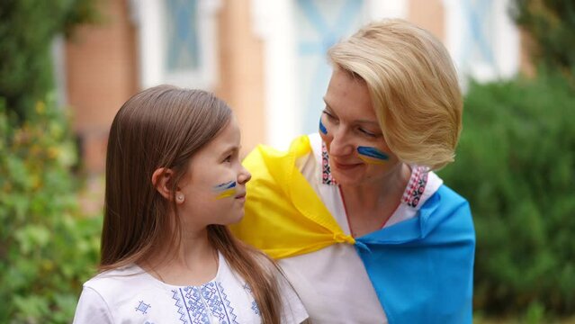 Pretty Ukrainian daughter and beautiful mother looking at each other smiling turning to camera in slow motion. Portrait of confident proud woman and girl with national flag face painting posing